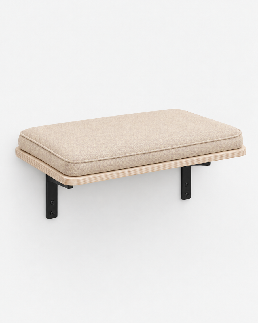 A wall-mounted birch plywood cat perch with two black brackets and a warm beige cushion, photographed on a plain light grey background.