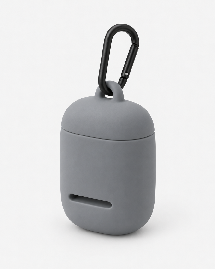 A small rounded silicone waste-bag pouch in mid cool grey with a magnetic lid, a front dispensing slot and a matte black carabiner, on a plain light grey background.
