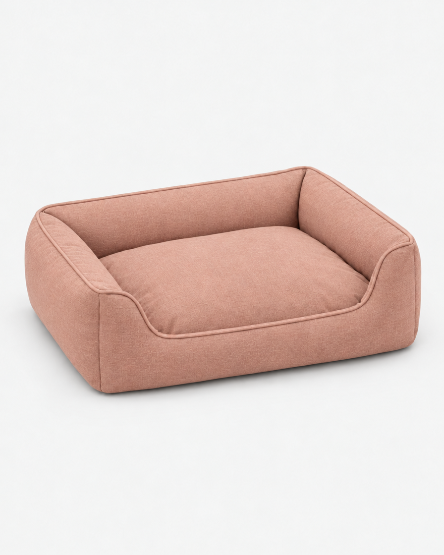 The same low bolster dog bed in a dusty terracotta pink woven fabric on a plain light grey studio background.