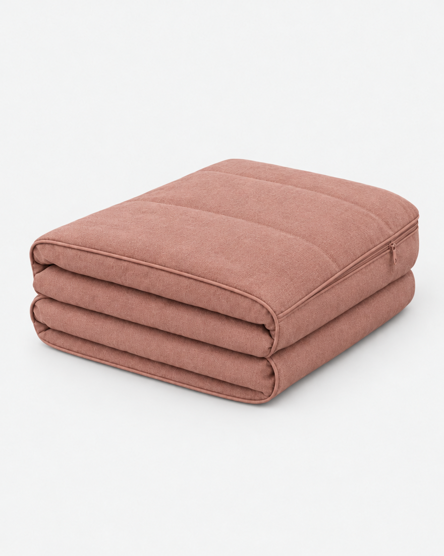 A washable dog bed cover in dusty terracotta pink, folded into a neat stack on a plain light grey background.