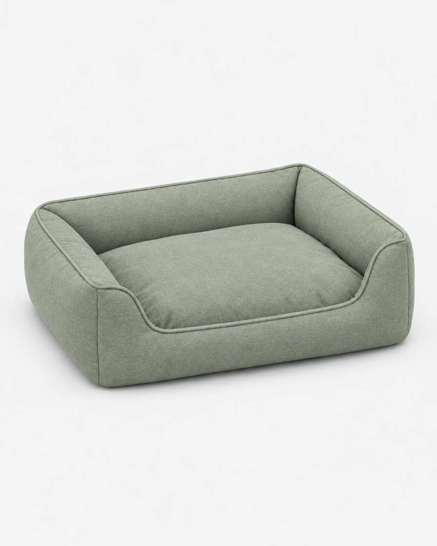 The same low bolster dog bed in a soft grey-green woven fabric on a plain light grey studio background.