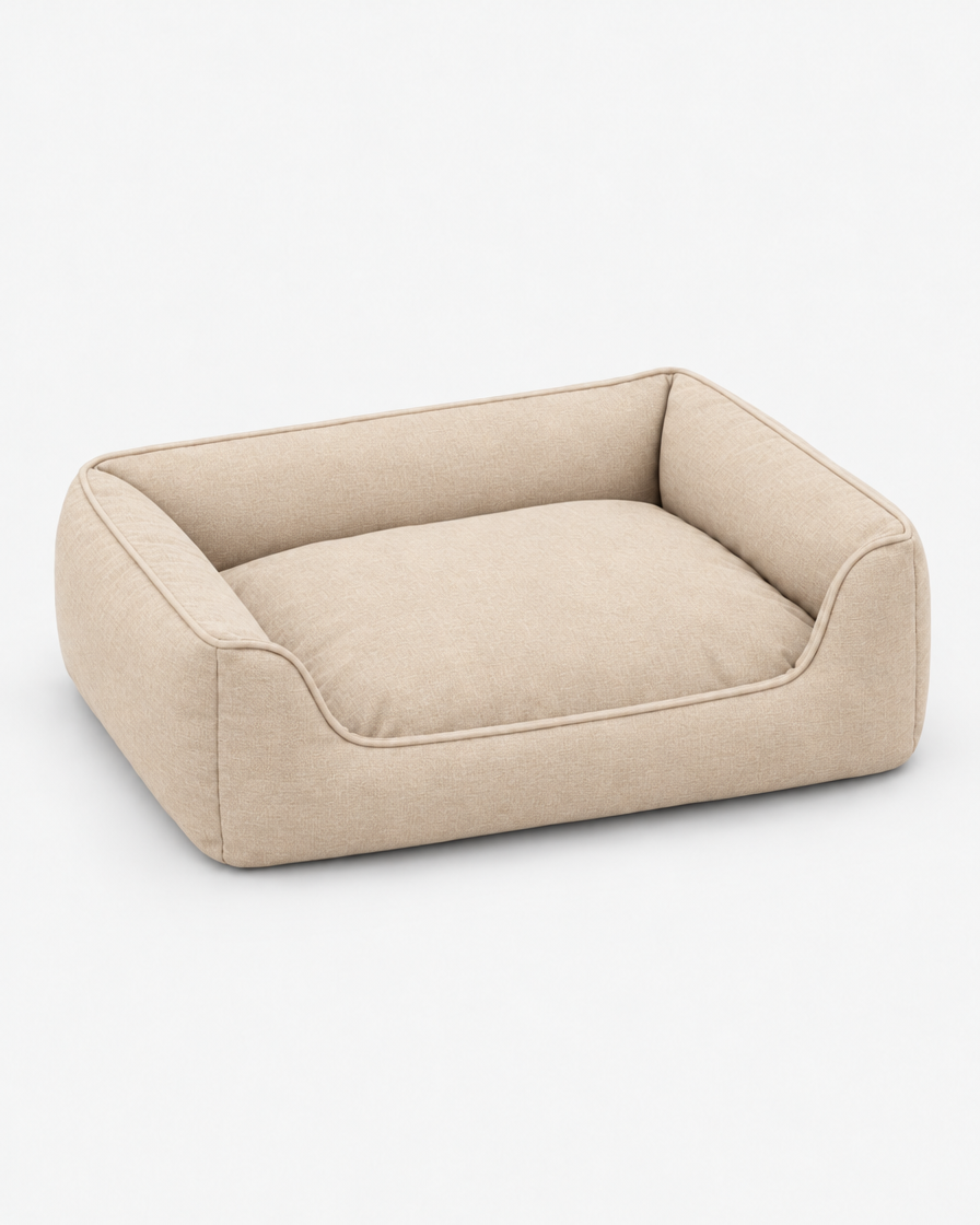The same low bolster dog bed in a warm beige woven fabric on a plain light grey studio background.