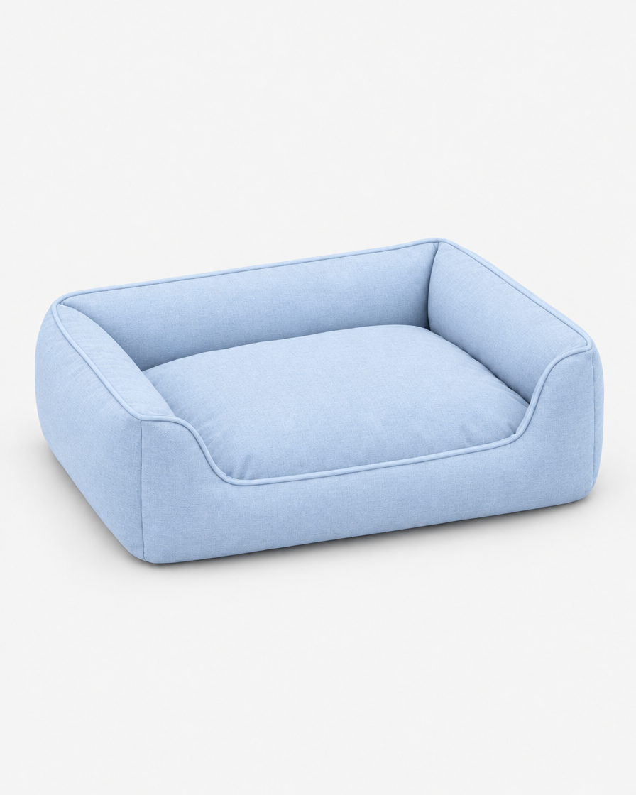 The same low bolster dog bed in a pale powder blue woven fabric on a plain light grey studio background.