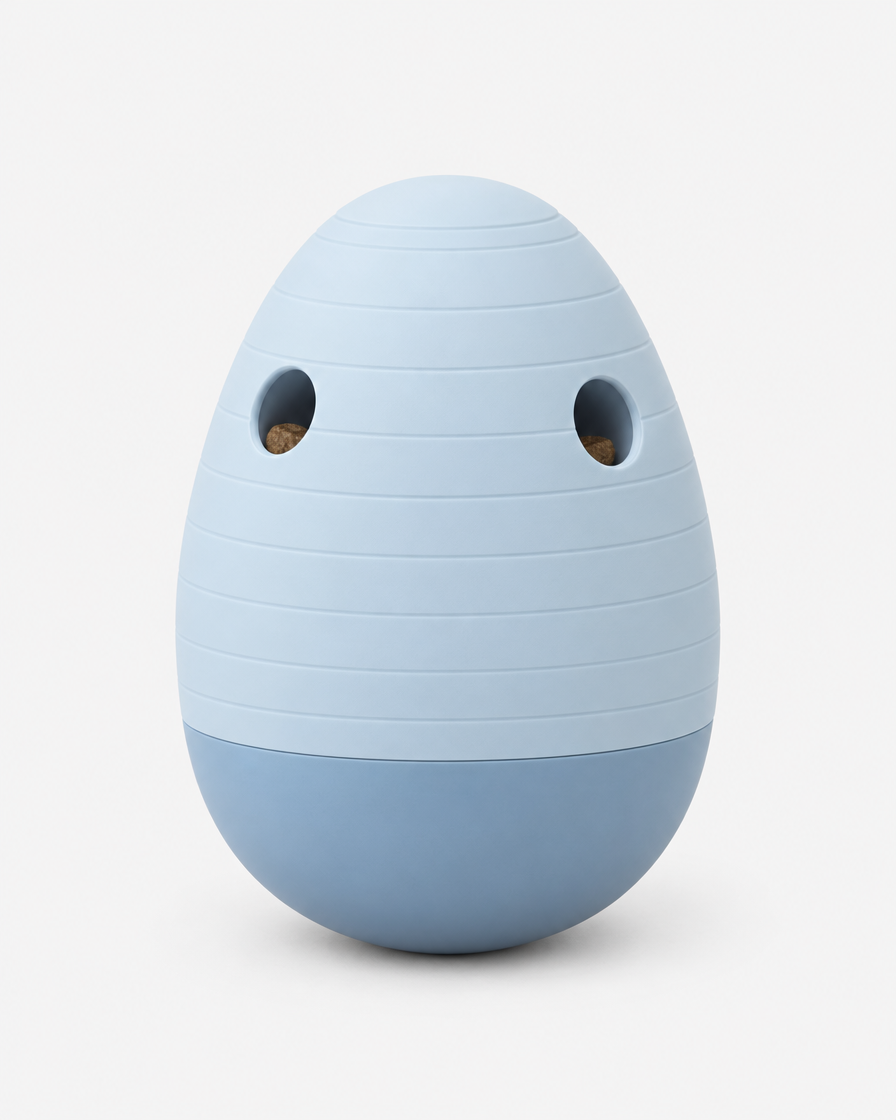 A pale powder blue egg-shaped puzzle feeder with horizontal grooves and two treat openings, standing on a light grey background.