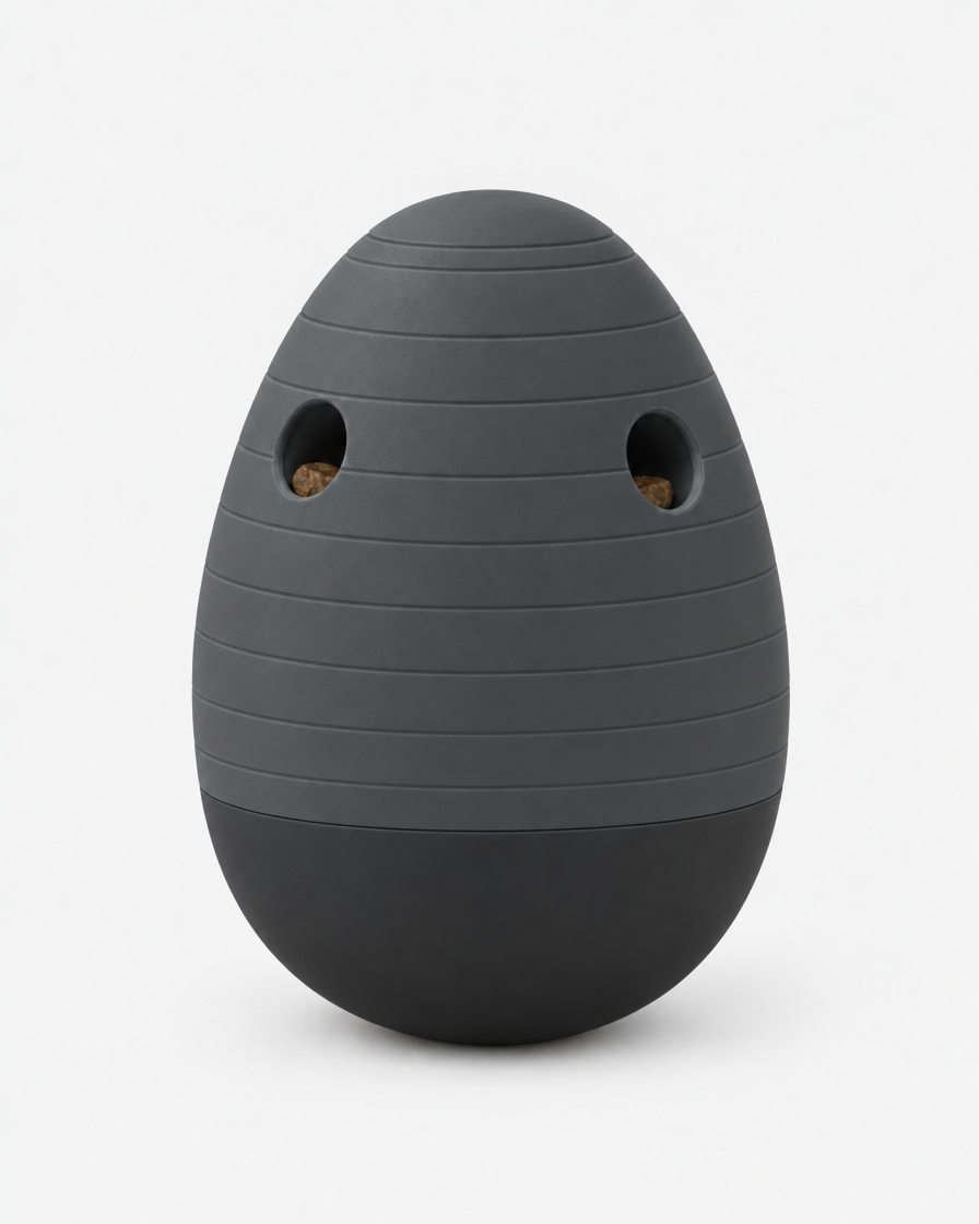 A dark charcoal grey egg-shaped puzzle feeder with horizontal grooves and two treat openings, standing on a light grey background.