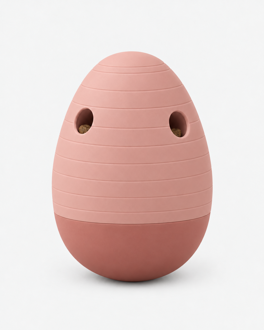 A dusty terracotta pink egg-shaped puzzle feeder with horizontal grooves and two treat openings, standing on a light grey background.