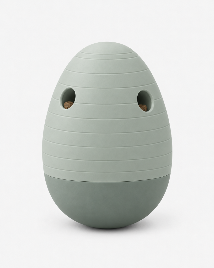 A soft grey-green egg-shaped puzzle feeder with horizontal grooves and two treat openings, standing on a light grey background.