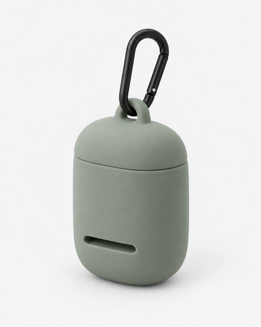 A small rounded silicone waste-bag pouch in soft grey-green with a magnetic lid, a front dispensing slot and a matte black carabiner, on a plain light grey background.