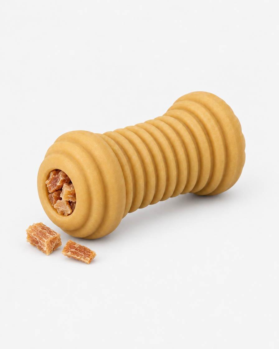 The ridged rubber chew toy with its hollow core stuffed with small dried chicken treats and two loose pieces beside it on a light grey background.
